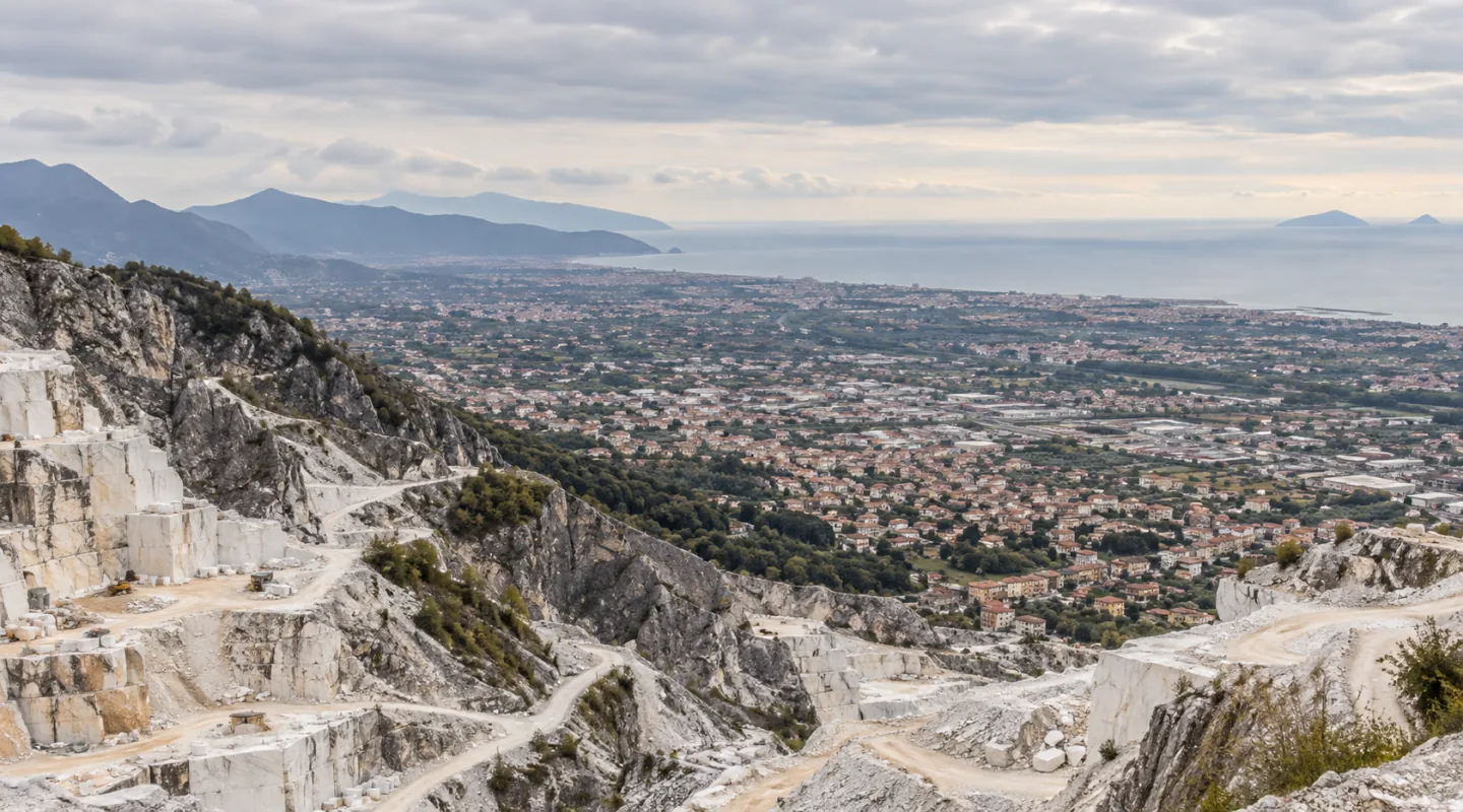 Veduta dall'alto di un bacino marmifero: terrazze di cava in primo piano, la pianura costruita e il mare all'orizzonte
